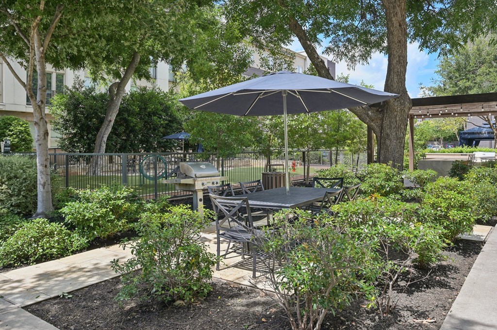 A patio with a table and chairs under an umbrella at Everra Midtown Park Apartments, Dallas, TX, 75231