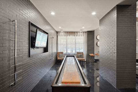 A room with a shiny wooden table in the middle and a television on the wall.