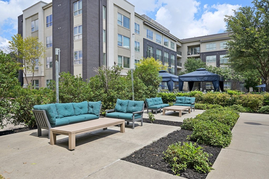 A modern outdoor seating area with blue cushioned sofas and a black umbrella at Everra Midtown Park Apartments, Dallas, TX