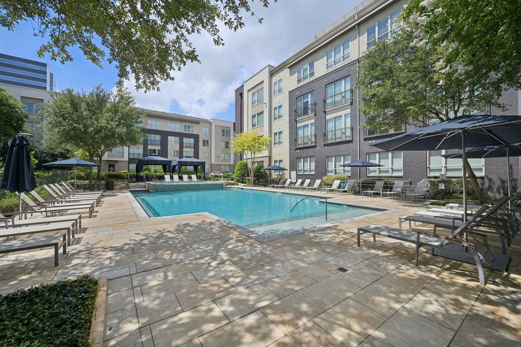A swimming pool surrounded by lounge chairs and umbrellas in a courtyard at Everra Midtown Park Apartments, Texas, 75231
