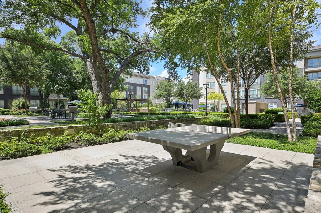 A concrete table is in the middle of a sunny park at Everra Midtown Park Apartments, Texas