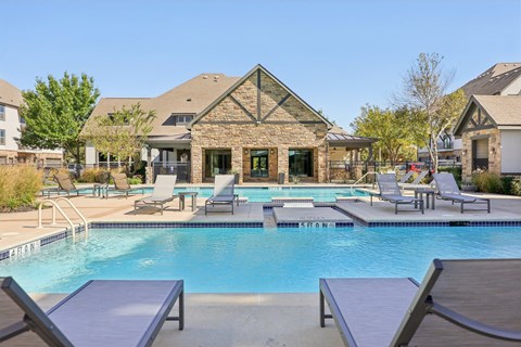 A pool with lounge chairs and a house in the background.