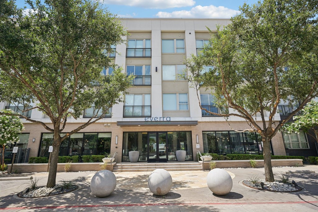 A modern building with a glass entrance and a tree in front at Everra Midtown Park Apartments, Dallas, TX