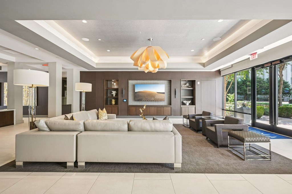 A modern living room with a large white sofa and a chandelier hanging from the ceiling at Everra Midtown Park Apartments, Texas