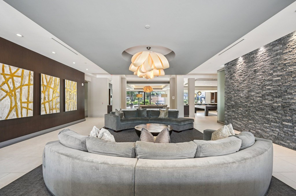 A modern living room with a large grey couch and a stone wall at Everra Midtown Park Apartments, Dallas, TX