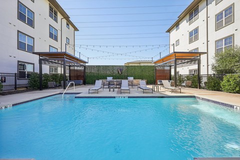 A swimming pool surrounded by chairs and buildings.