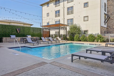 A pool with lounge chairs and a building in the background.
