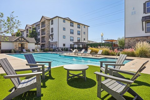 A poolside area with chairs and a table in front of apartment buildings.