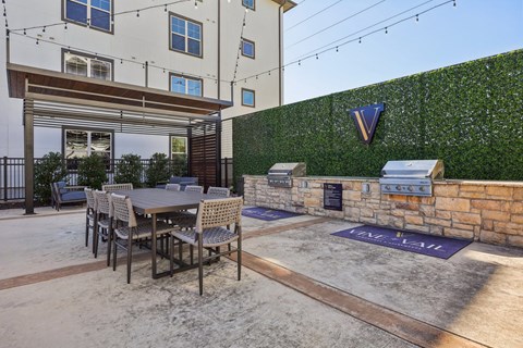 A patio with a table and chairs is surrounded by a wall with a green hedge.