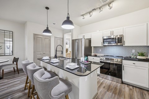 A modern kitchen with a black granite countertop and grey bar stools.