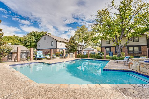 A swimming pool surrounded by a stone patio and a grassy area with trees.