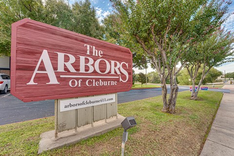A sign that says "The Arbors of Cleburne" is in front of some trees.