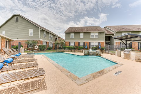 A swimming pool surrounded by sun loungers and apartment buildings.