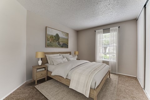 A bedroom with a bed, nightstand, and a painting on the wall.