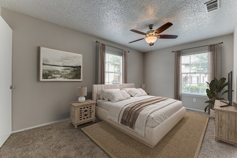 A bedroom with a large bed, a ceiling fan, and a painting on the wall.