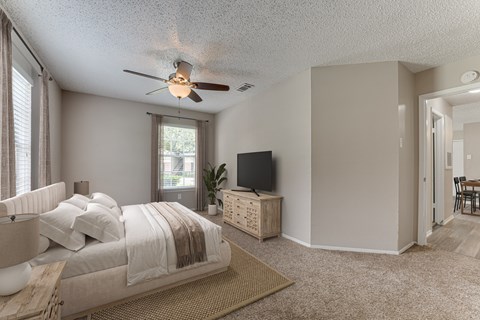 A bedroom with a bed, a television, and a ceiling fan.