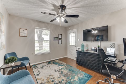 A living room with a ceiling fan, a blue chair, a black cabinet, and a television.