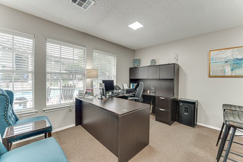 A room with a desk, chairs, and a window with blinds.