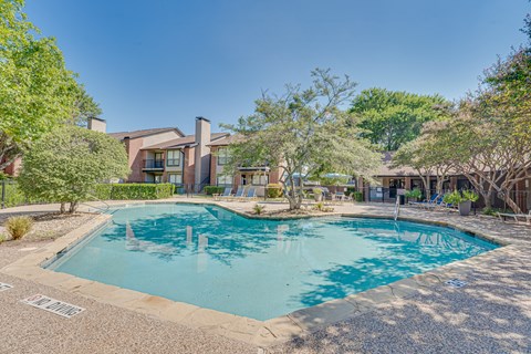 A swimming pool surrounded by a gravel area and trees.