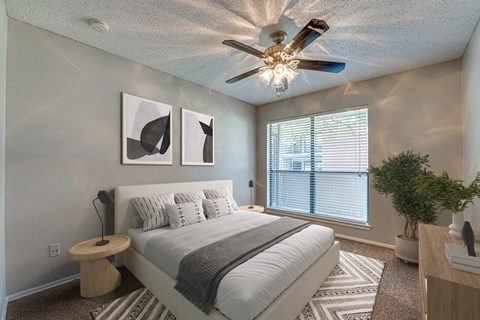 A bedroom with a bed, a ceiling fan, and a window with blinds.
