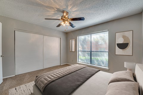 A bedroom with a bed, a ceiling fan, and a window with blinds.