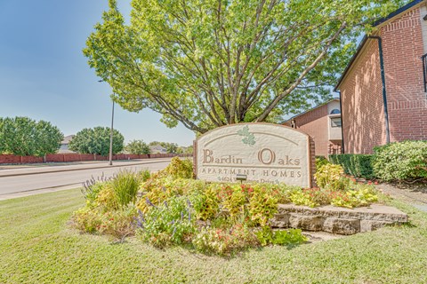A sign for Bardin Oaks Apartment Homes is surrounded by greenery.