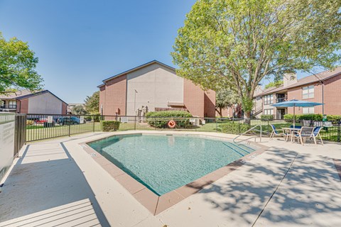A small pool in a courtyard surrounded by chairs and trees.