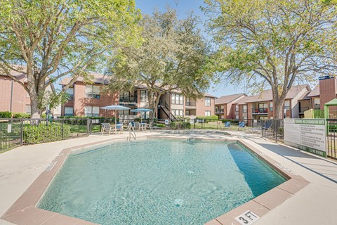 A swimming pool surrounded by trees and apartment buildings.