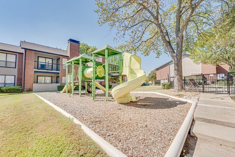 A playground with a green and yellow slide in front of a building.