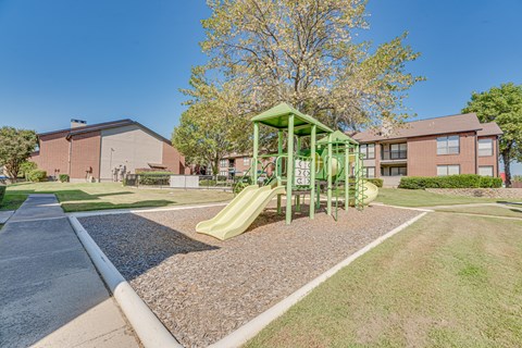 A playground with a green slide in front of a red brick building.