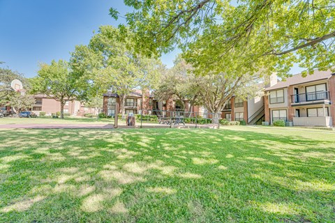 A sunny day at a park with a basketball court and green grass.