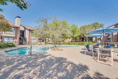 A pool surrounded by chairs and trees in a sunny backyard.
