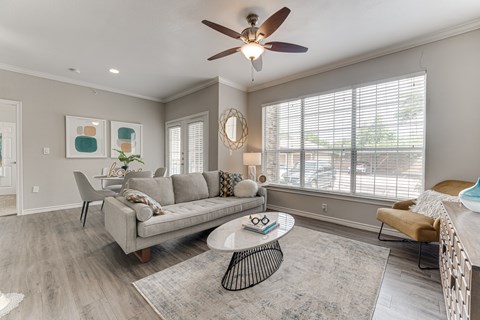 A living room with a grey couch, a round table, and a ceiling fan. at The Brazos, Dallas