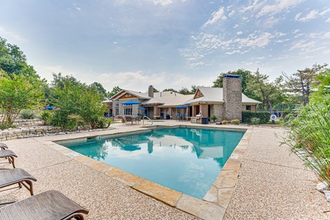 A large outdoor swimming pool surrounded by a stone patio and lounge chairs.
