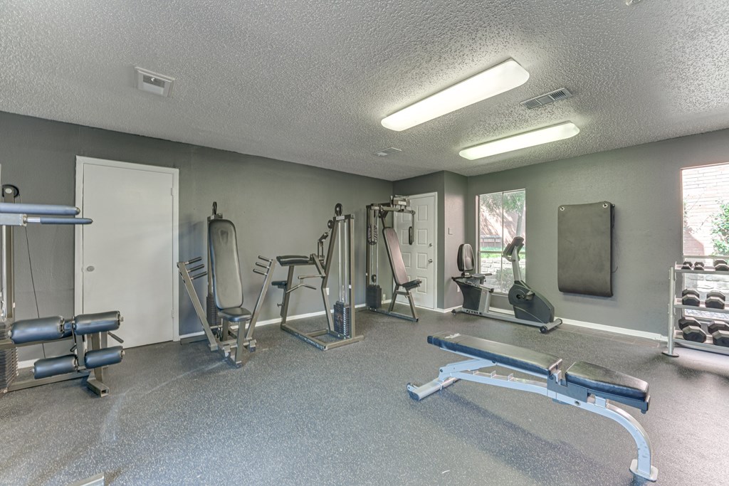 A gym with a variety of equipment including a bench press, a squat rack, and a leg press machine at Copper Hill Apartments, Texas