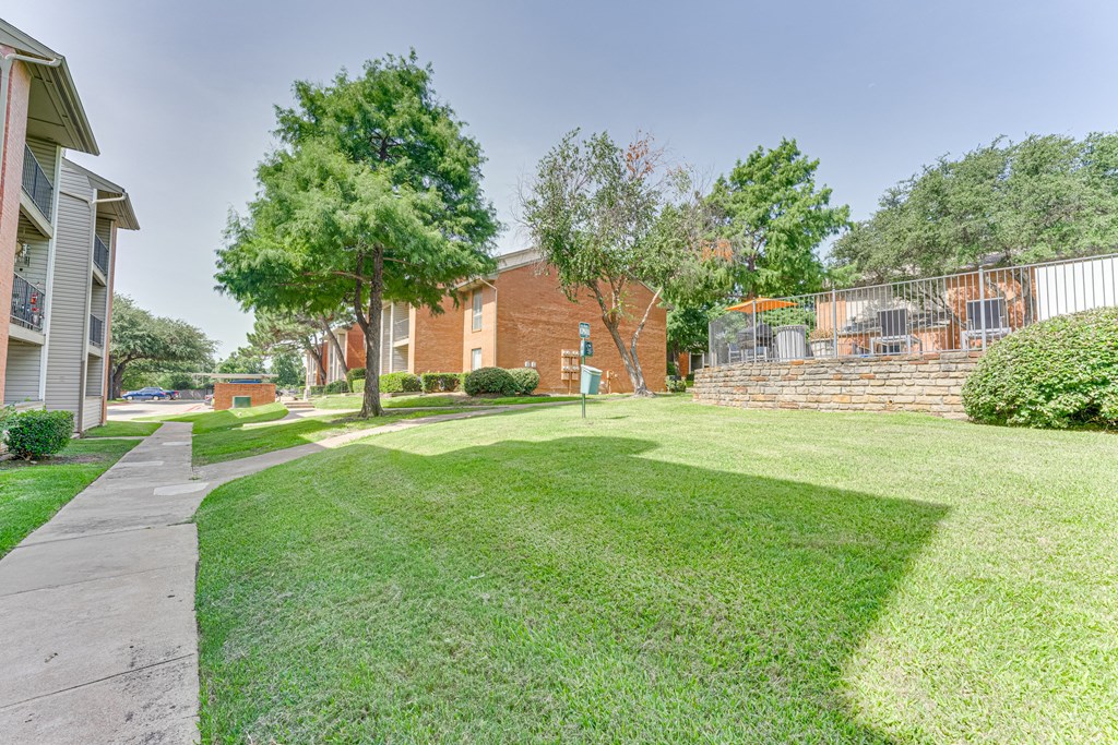 A grassy area with a sidewalk and a building in the background at Copper Hill Apartments, Bedford, Texas