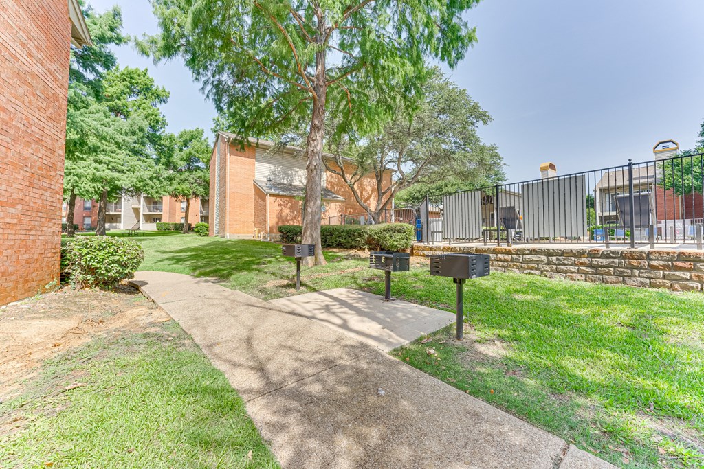 A tree stands in a grassy area in front of a brick building at Copper Hill Apartments, Bedford, TX, 76021