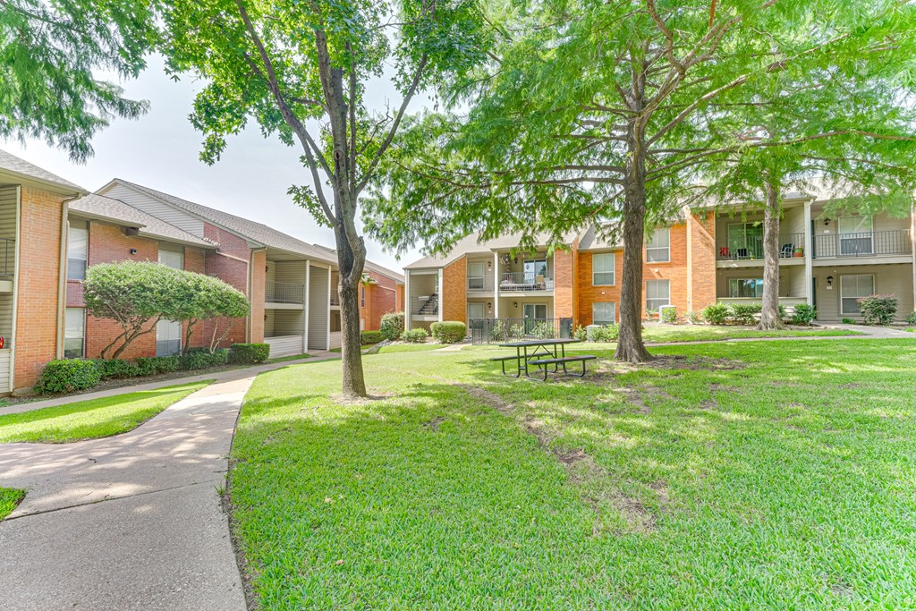 A grassy area with a bench and trees in front of apartment buildings at Copper Hill Apartments, Bedford