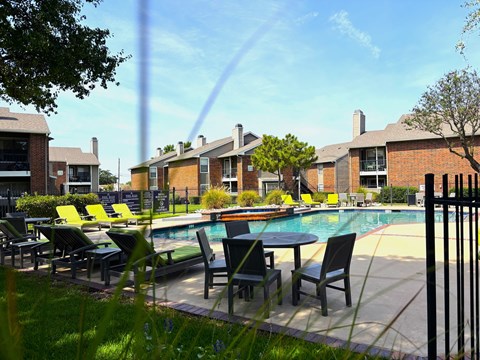 A pool surrounded by chairs and tables in front of a building.