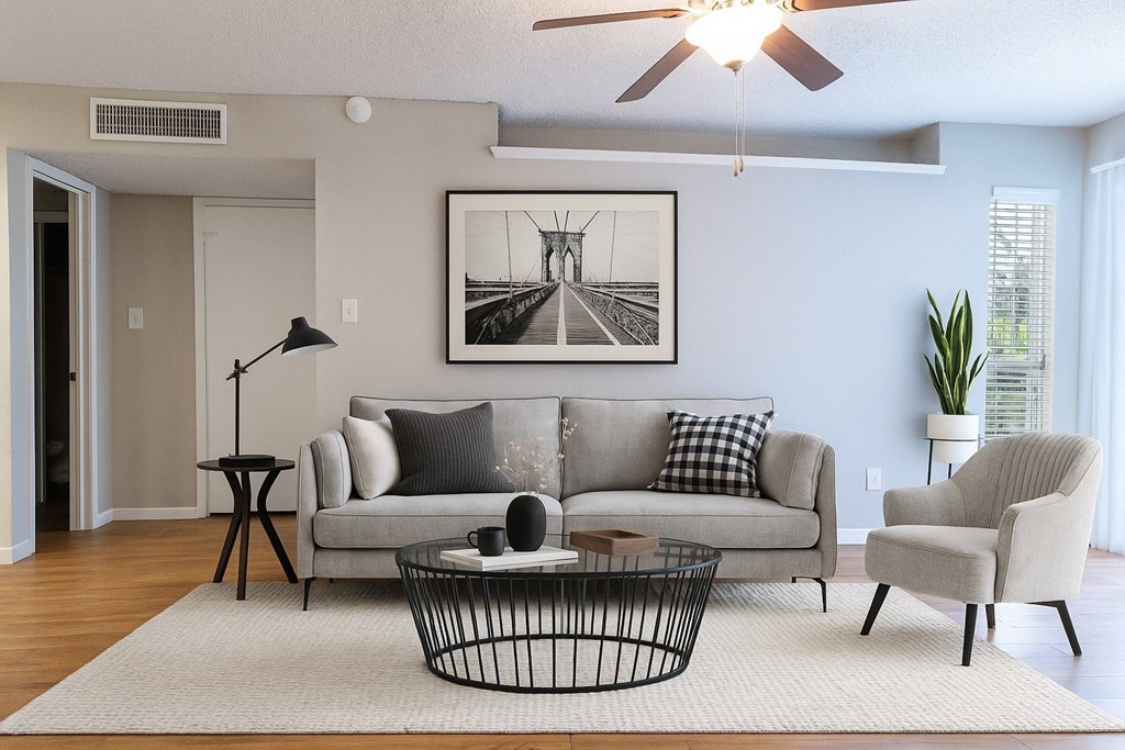A living room with a grey couch, a black floor lamp, a small table, a coffee table, a chair, a potted plant, and a framed picture on the wall.