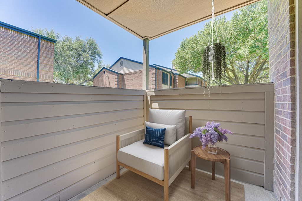 A wooden chair with a cushion and a small table with flowers on it. at Indian Creek Apartments, Carrollton, TX, 75007