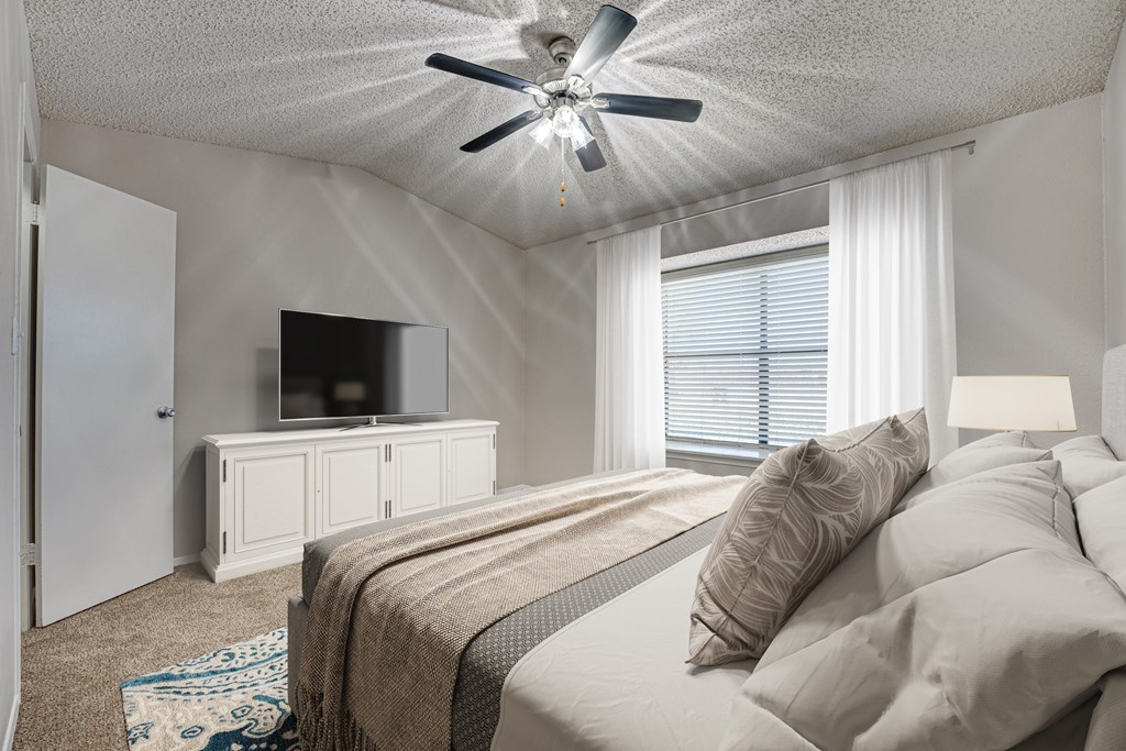A bedroom with a bed, a television, and a ceiling fan at Indian Creek Apartments, Carrollton, TX