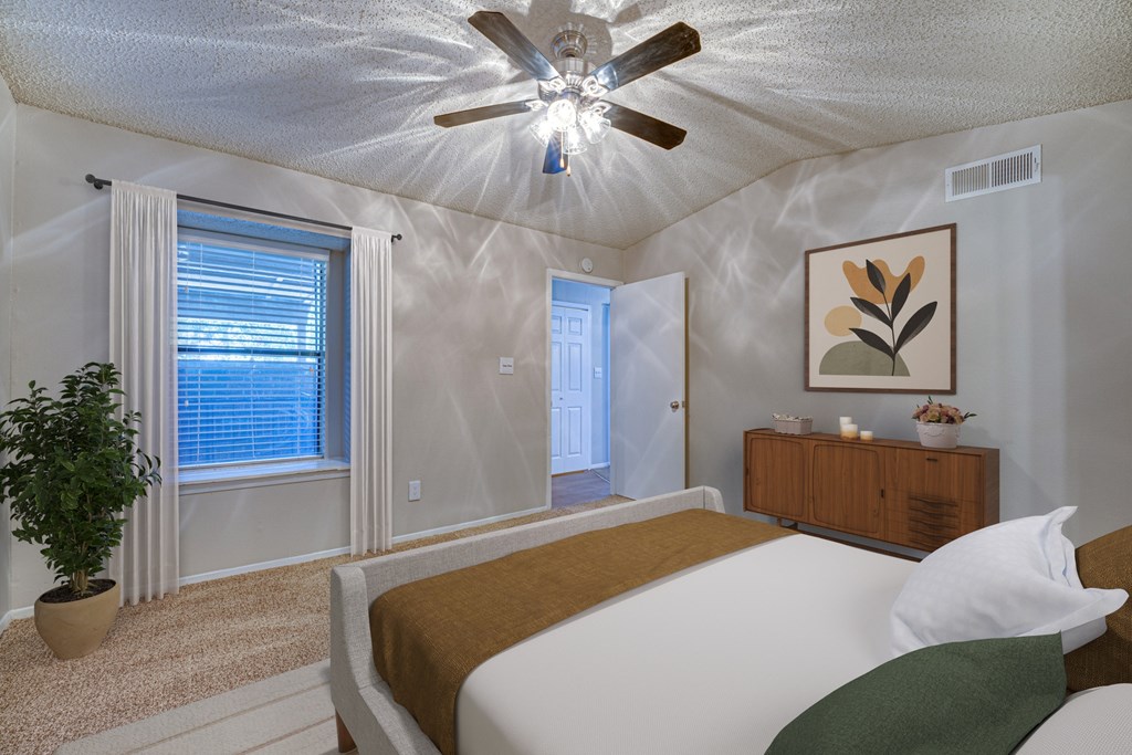 A bedroom with a bed, a ceiling fan, and a plant at Indian Creek Apartments, Carrollton, TX