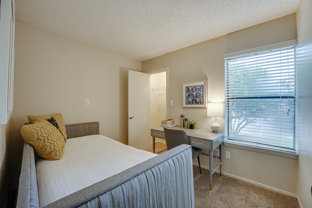 a bedroom with a bed and a desk and a window at Indian Creek Apartments, Carrollton