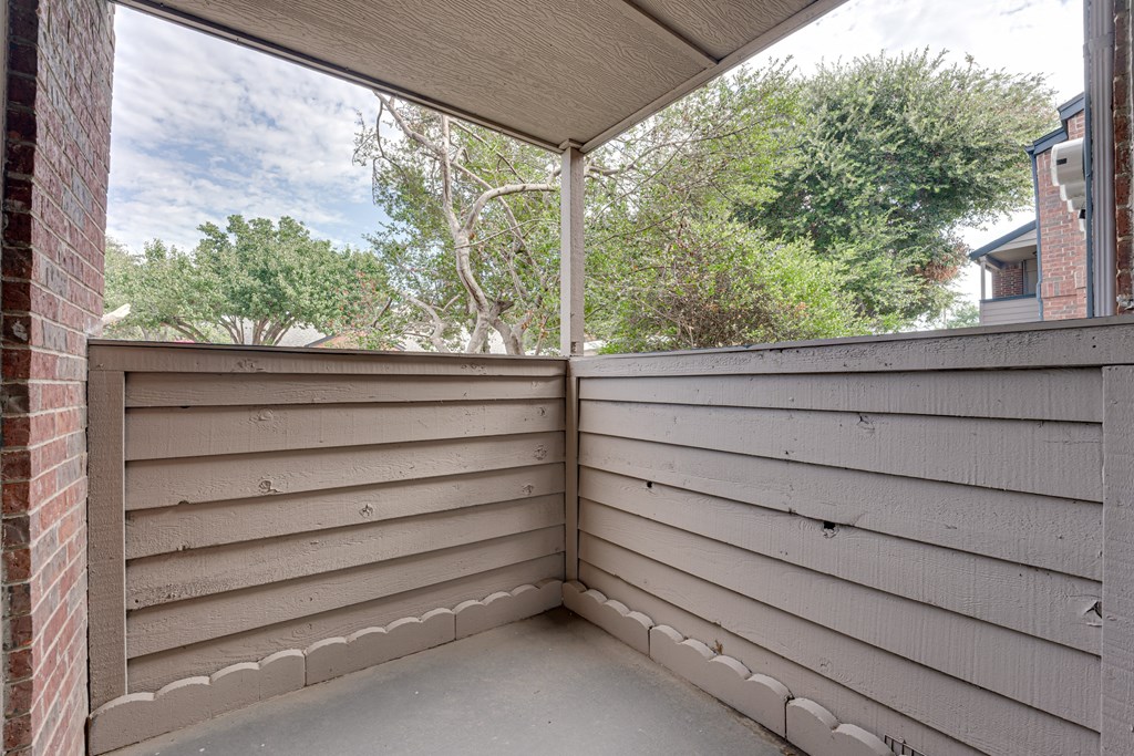 a covered porch with a view of trees and a brick house at Indian Creek Apartments, Carrollton, 75007