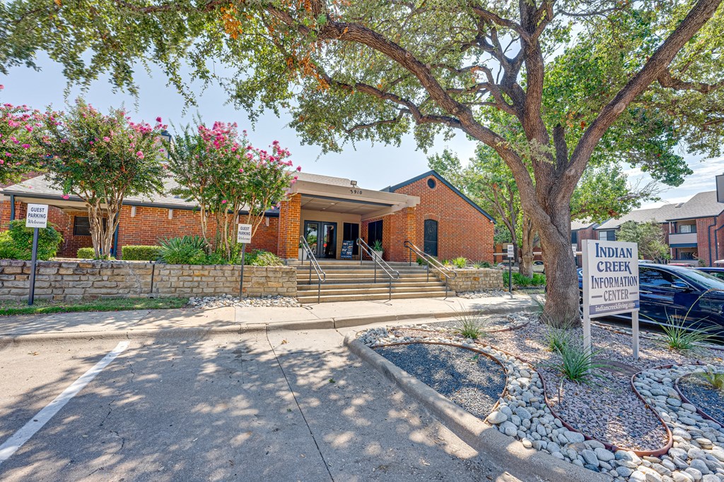 a building with a sign in front of it and a tree at Indian Creek Apartments, Carrollton, Texas