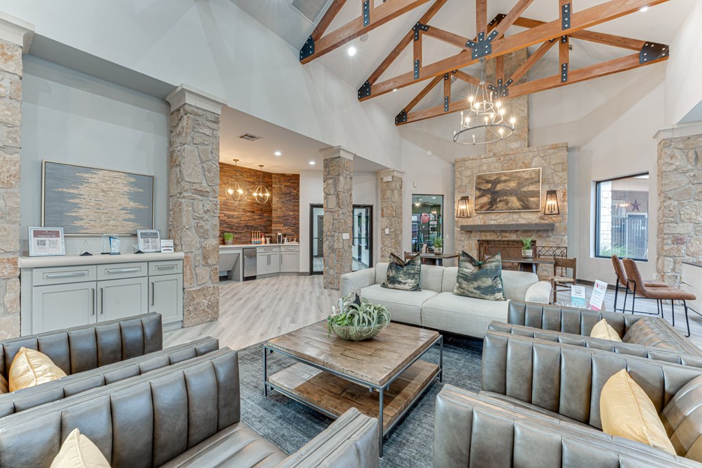 A large, modern living room with a stone fireplace and a high ceiling with exposed beams at Limestone Ranch Apartments, Texas, 75067