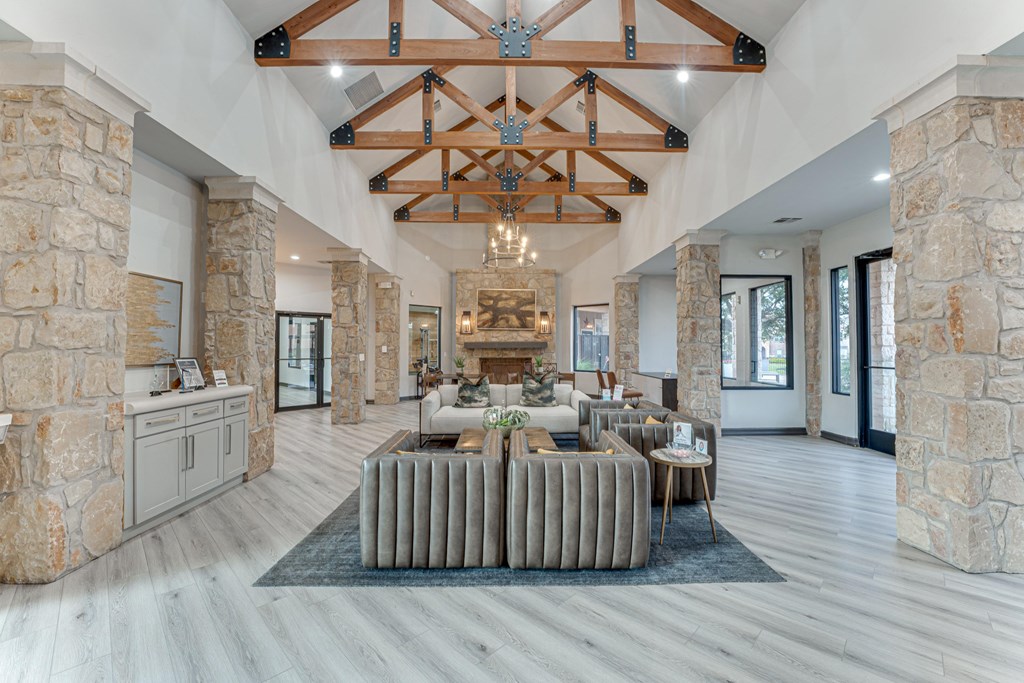 A spacious living room with a stone wall and a large wooden beam ceiling at Limestone Ranch Apartments, Texas, 75067