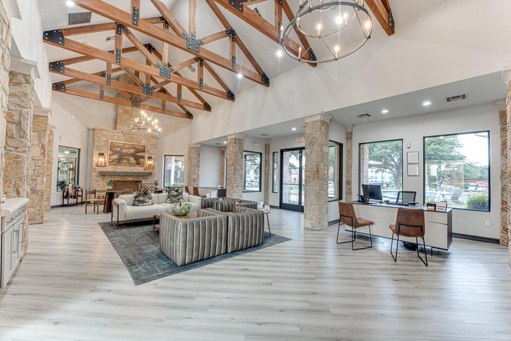 A spacious living room with a stone fireplace and a large wooden beam ceiling at Limestone Ranch Apartments, Texas