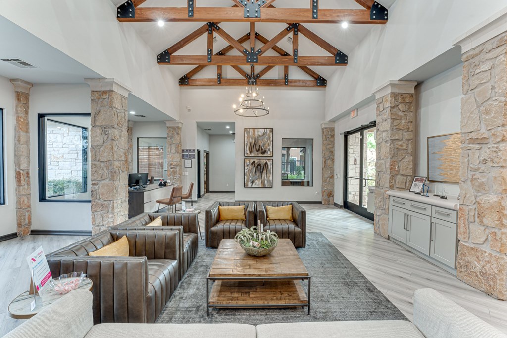 A large, open living room with a stone wall and a wooden beam ceiling at Limestone Ranch Apartments, Lewisville, TX, 75067